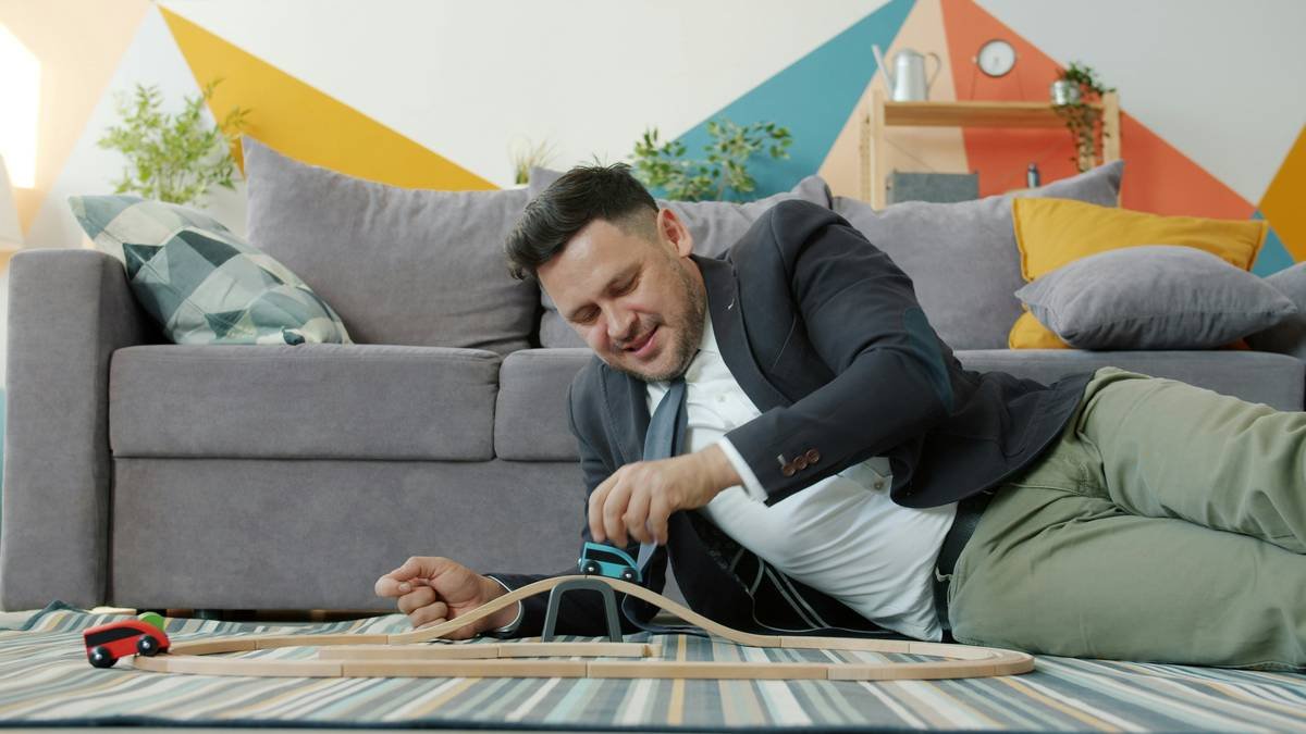 Cheerful businessman handsome middle-aged man is playing with cars at home relaxing having fun alone. Businesspeople, free time and relaxation concept.
